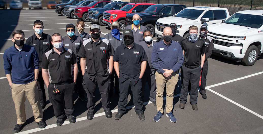 Student and instructors stand beside new trucks.