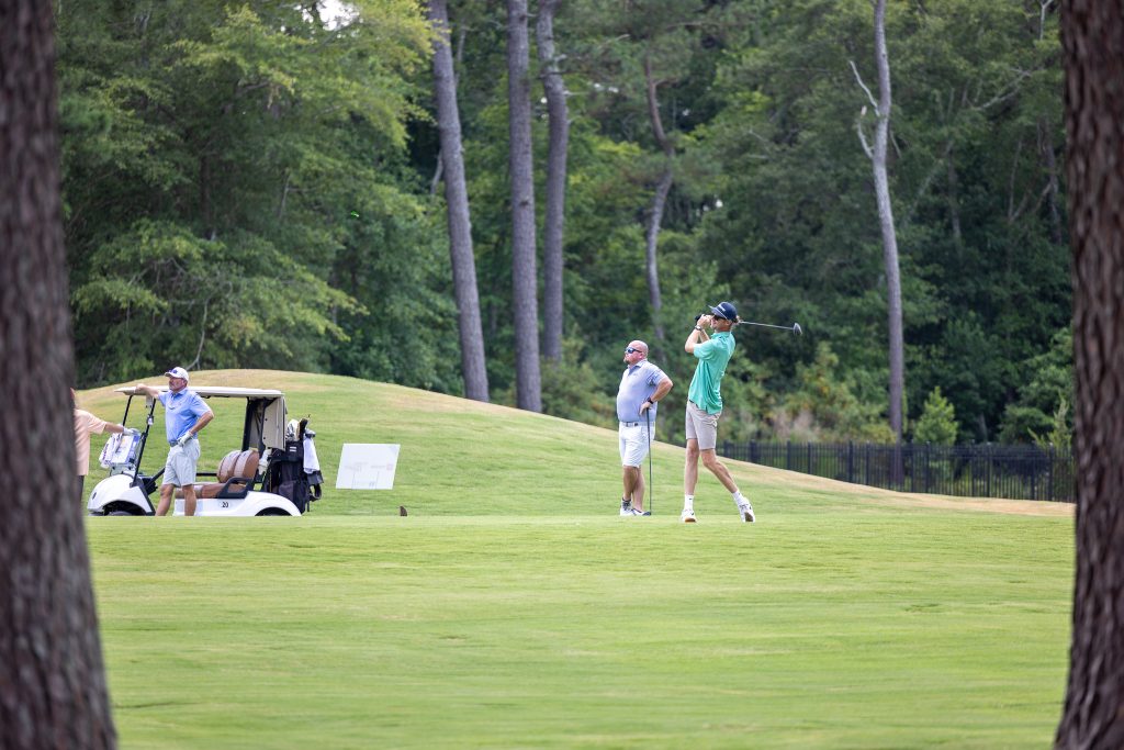A man swings a golf club while two other men stand on the course and watch.