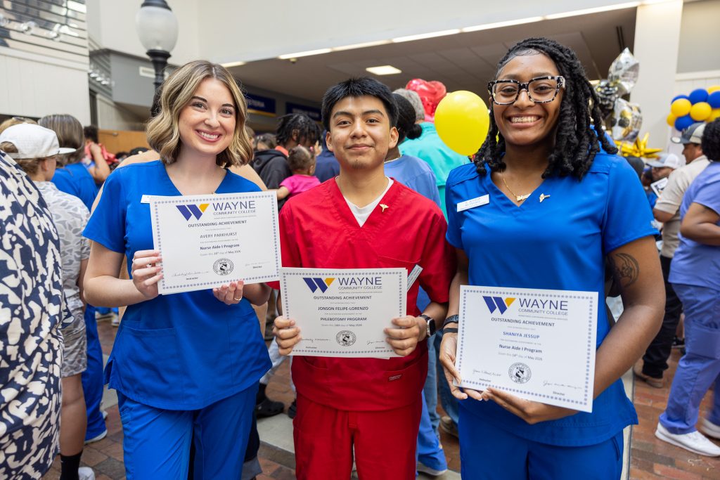 Students wearing medical scrubs stand together holding certificates.
