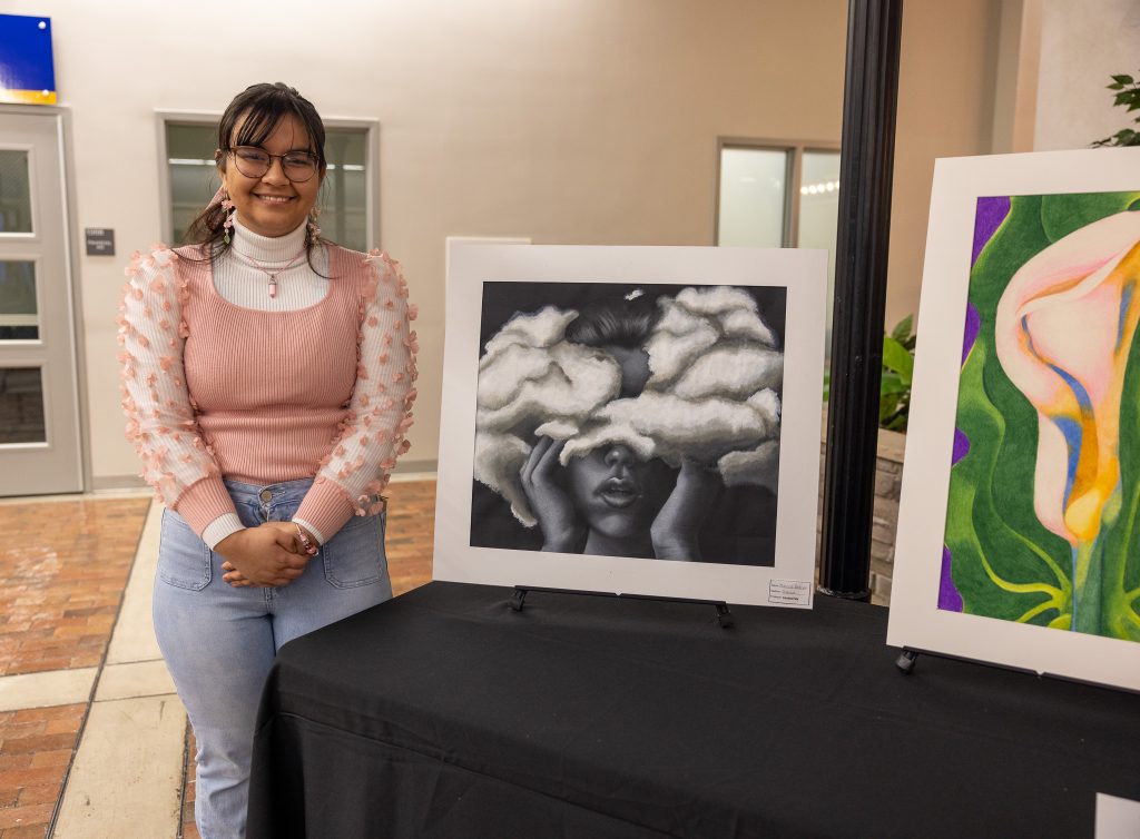 A student stands next to a piece of artwork sitting on a table.