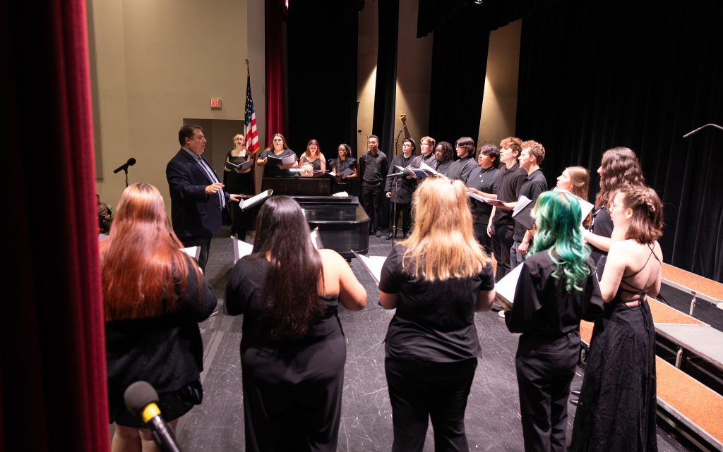 Students stand in a semicircle on stage.