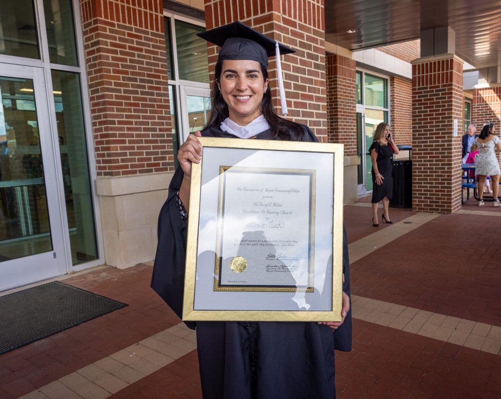 A woman wearing a graduation cap and gown holds a framed certificate.