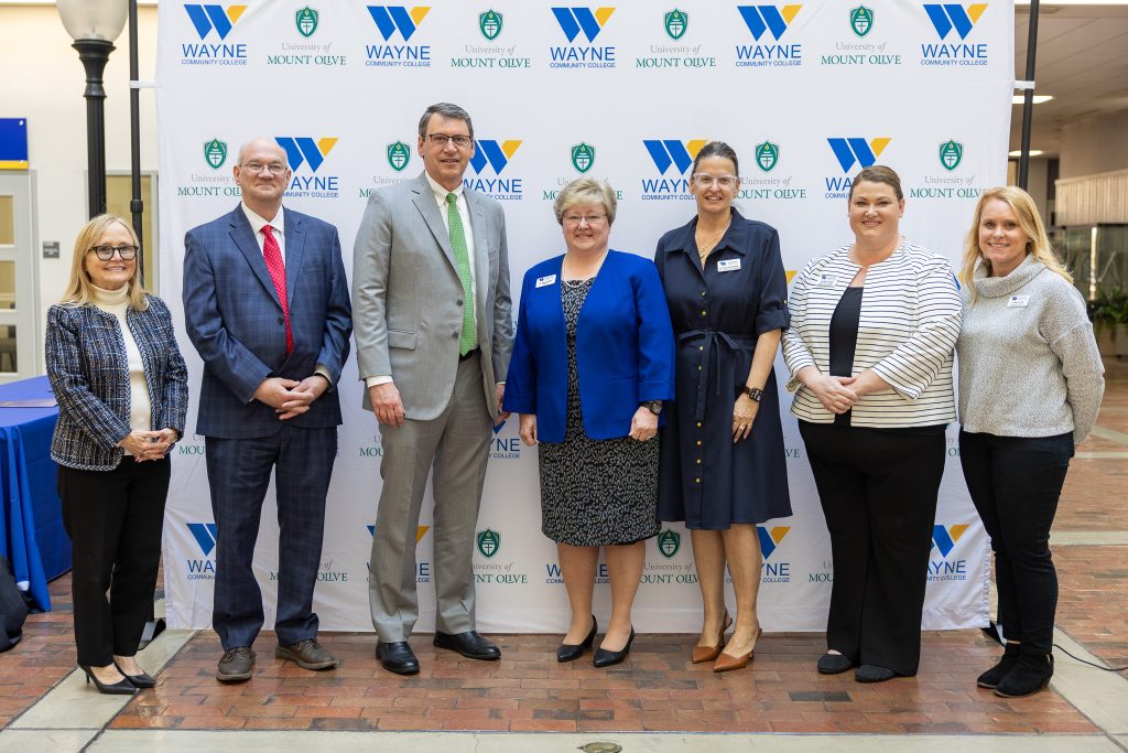 Individuals stand together in front of a backdrop.