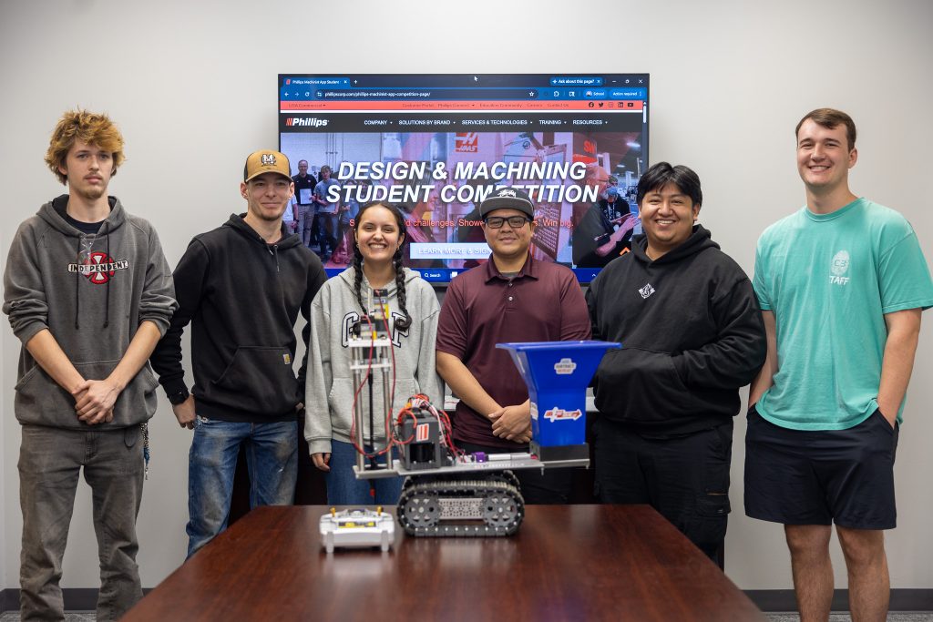 Students stand together behind a small machine.