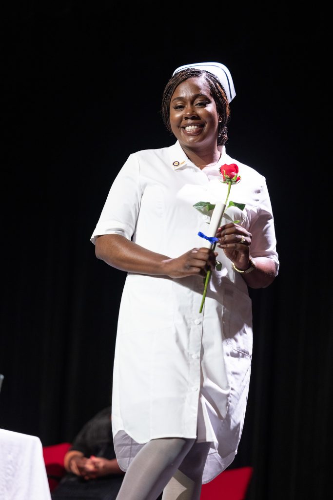 A woman wears a traditional white nursing uniform and holds a rose.