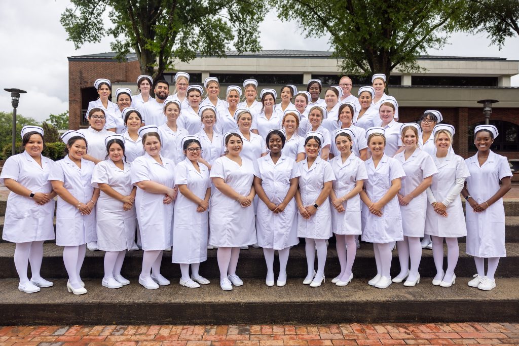 Nurses stand together wearing traditional white nursing uniforms.