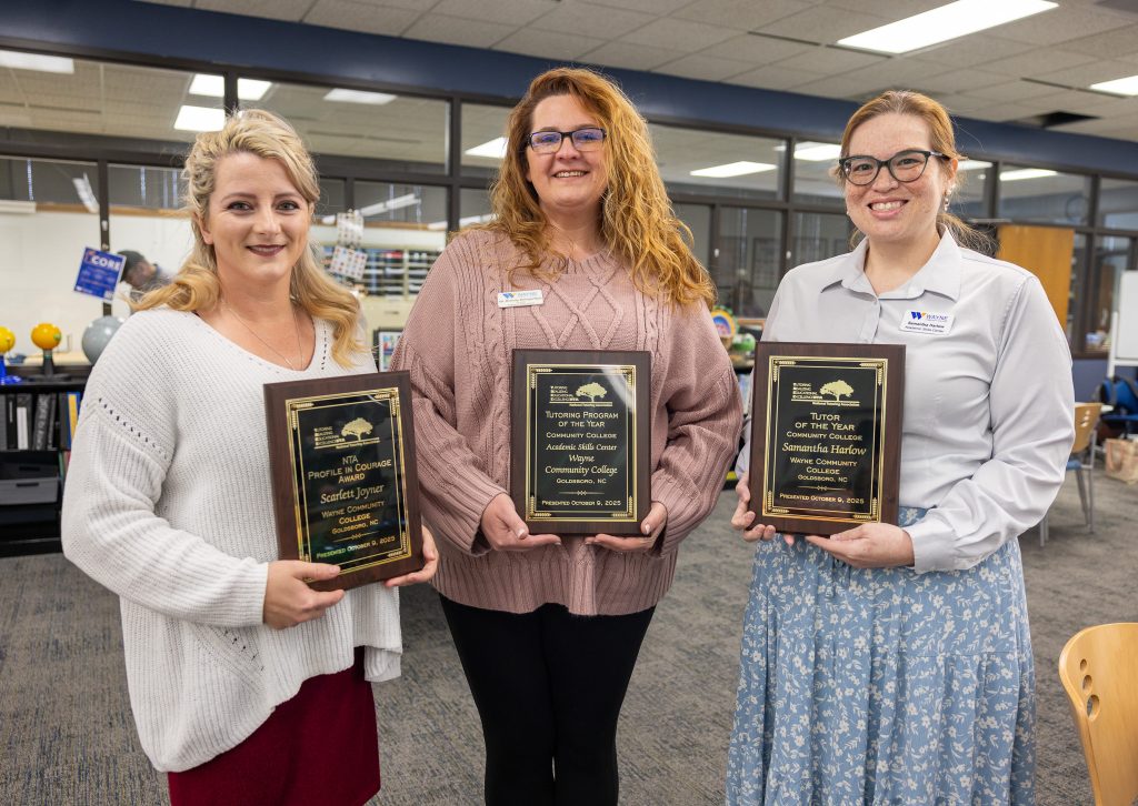 Three women stand together holding plaques.