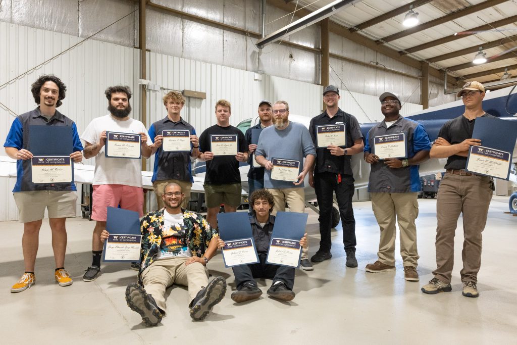 Individuals stand together in an airplane hangar holding certificates.