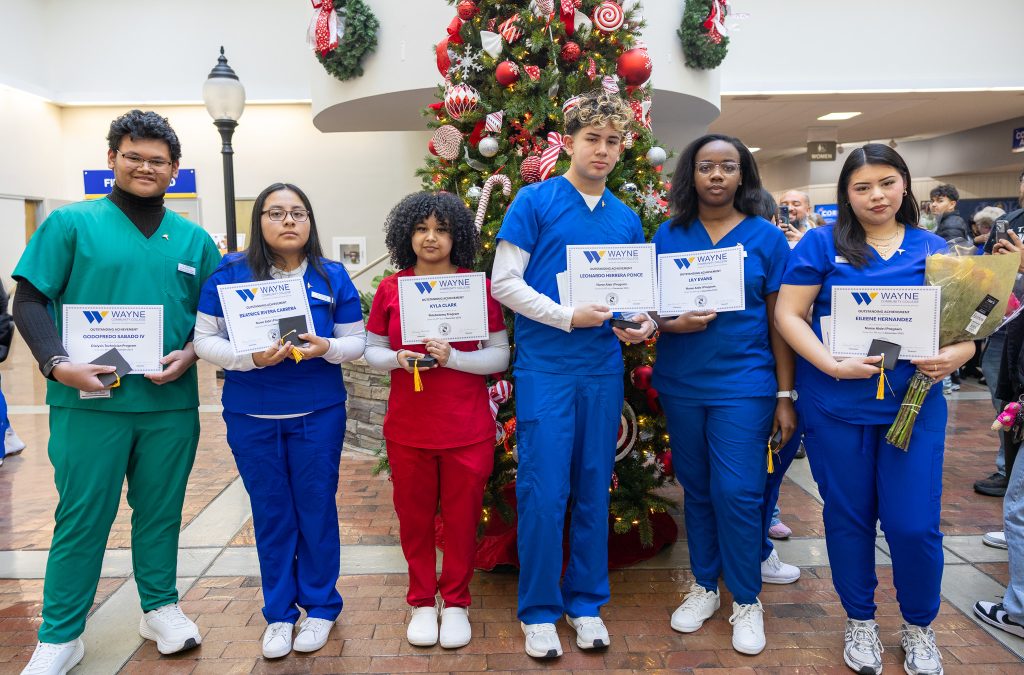 Individuals stand together wearing medical scrubs and holding certificates.