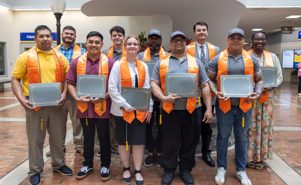 Individuals wearing orange graduation stoles and cords hold certificates.