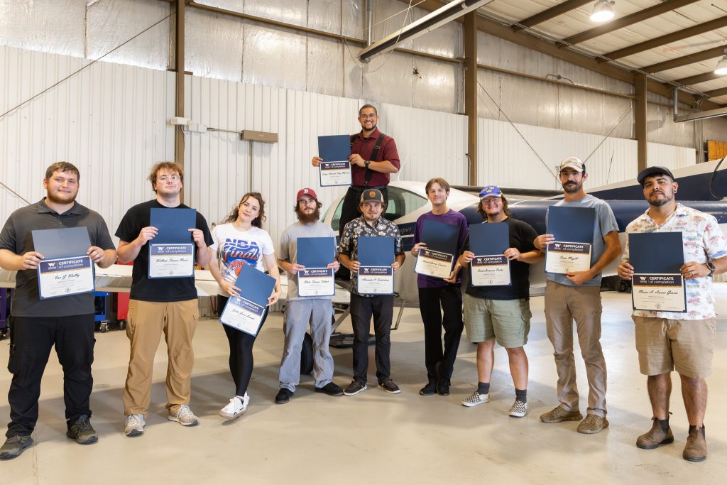 Individuals stand together in an airplane hangar holding certificates. 