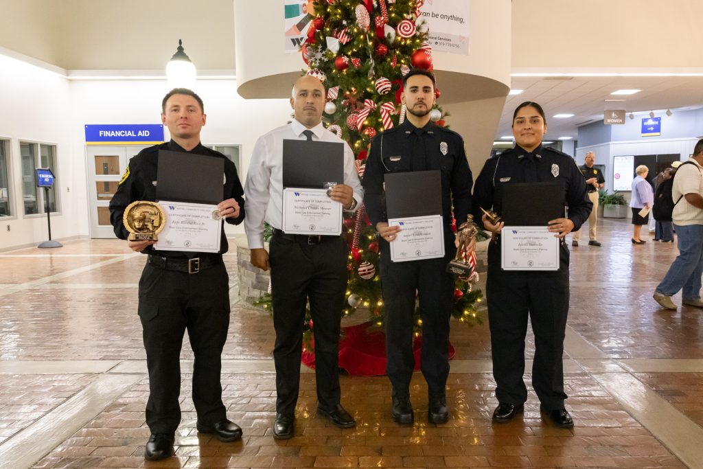 Four individuals hold certificates while standing in front of a Christmas tree.