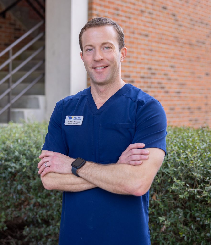 A man wearing medical scrubs stands with his arms crossed.