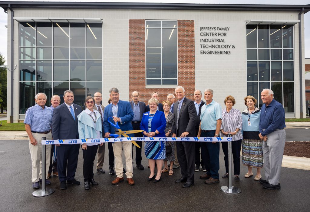 A group of people stand in front of a building while one of them cuts a ribbon with scissors.