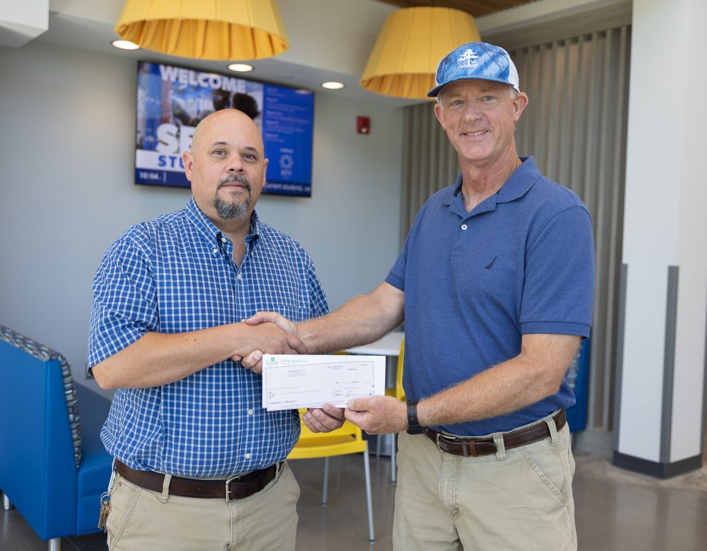 Two men hold a check while shaking hands.