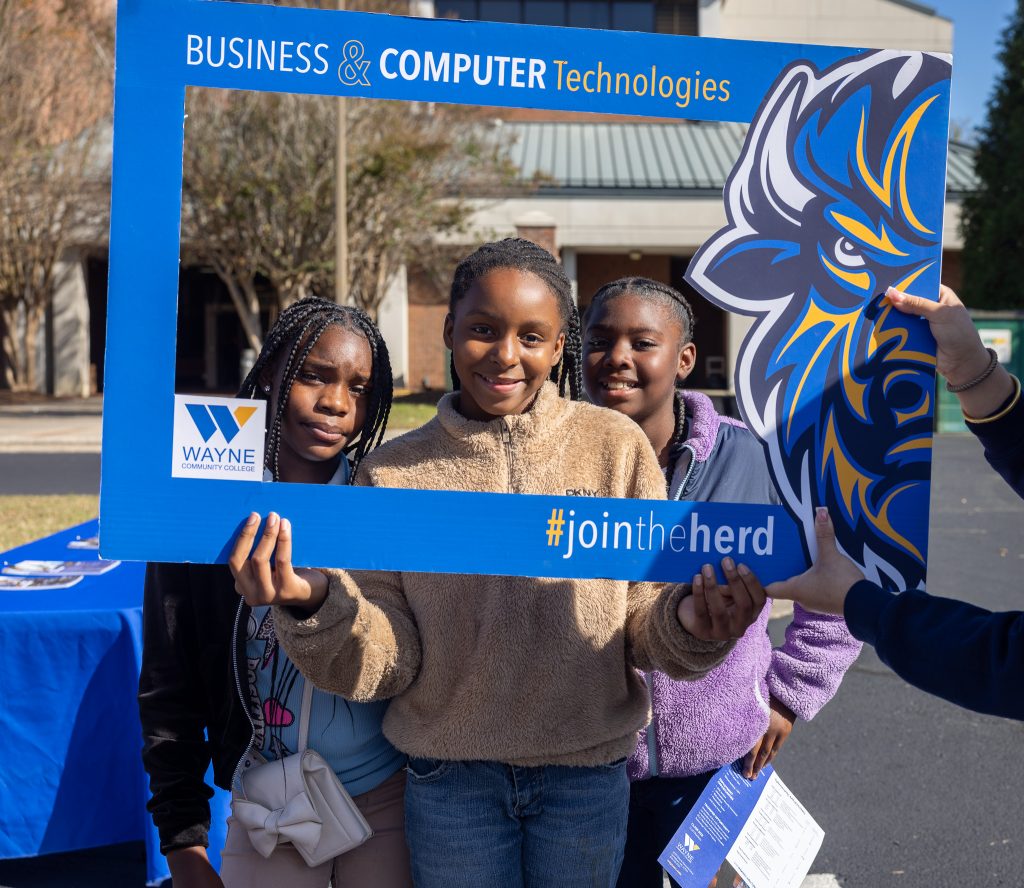 Three students stand behind a cut-out frame.