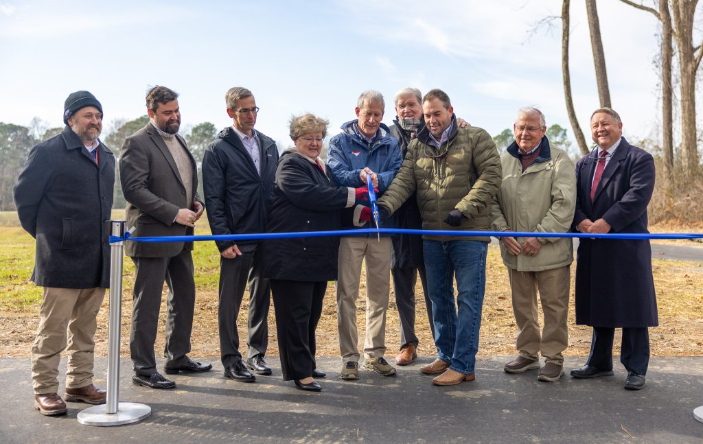 Individuals stand together and cut a ribbon with scissors.