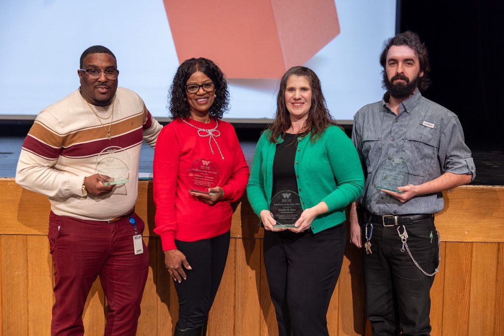 Four individuals stand together holding plaques.