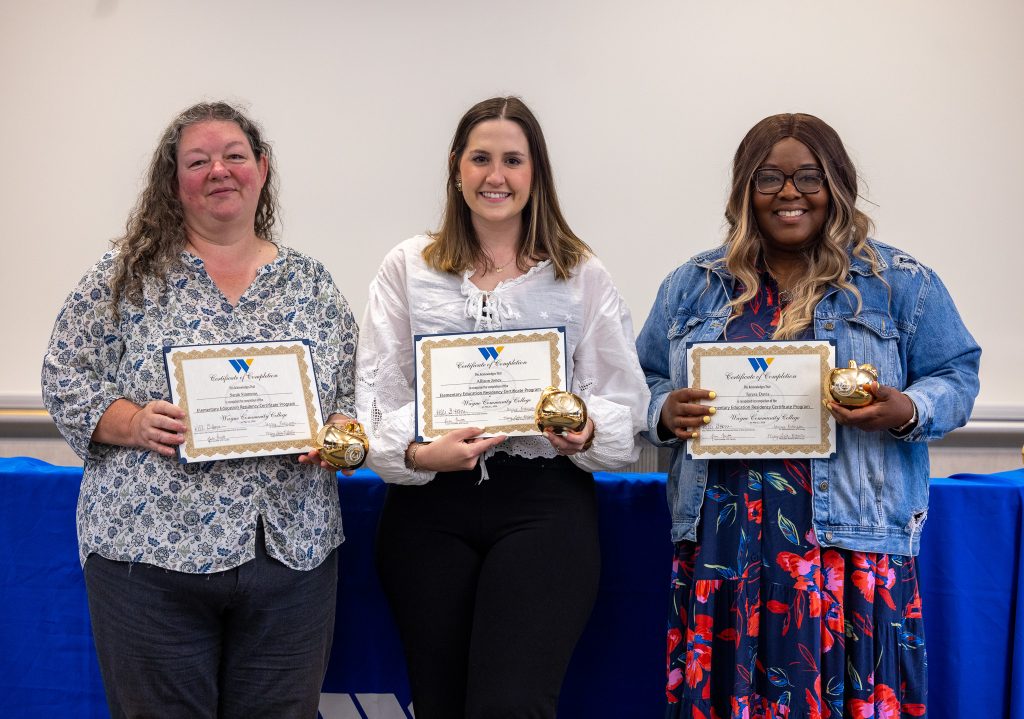 Three women stand together holding certificates.