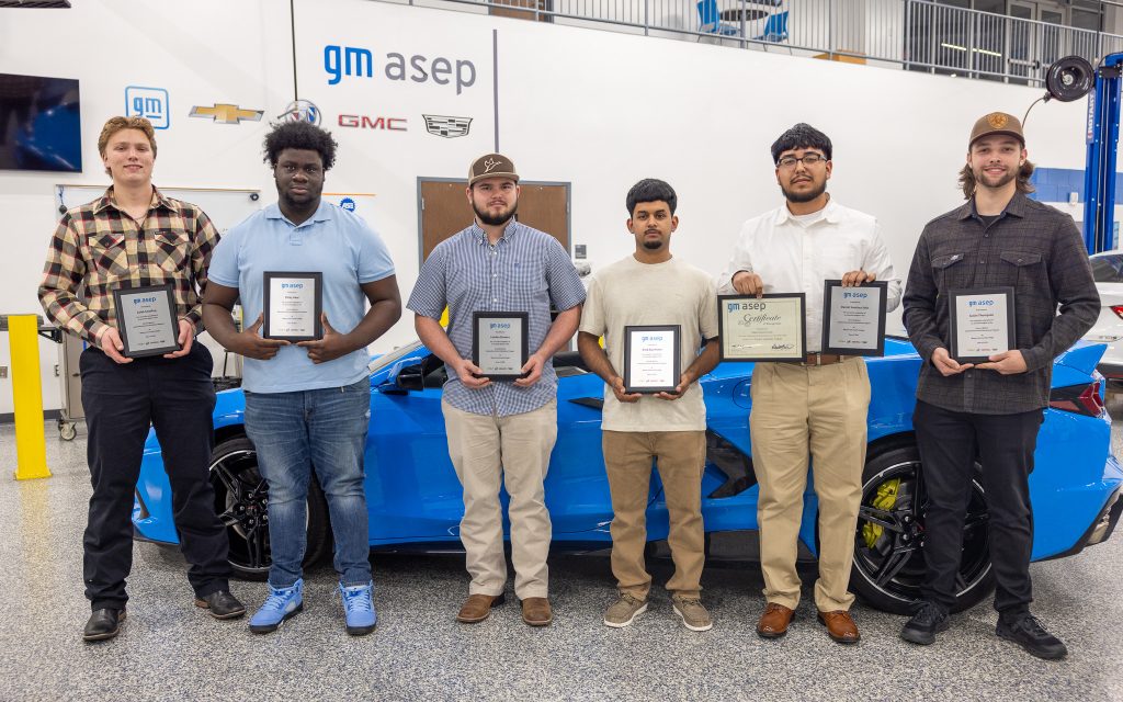 Individuals hold plaques while standing in front of a blue Corvette.