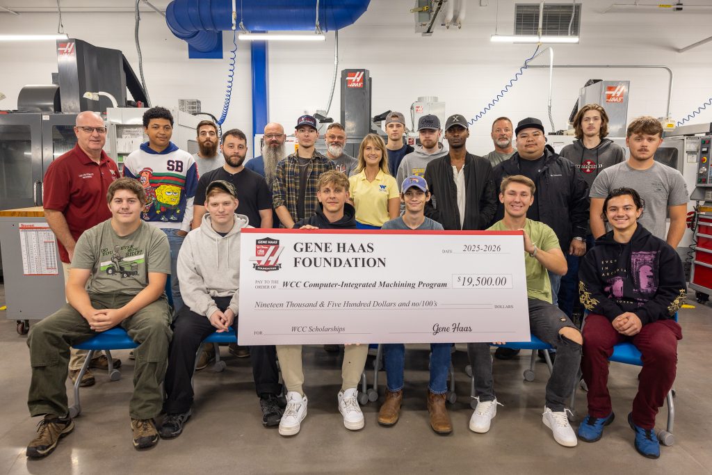 Individuals are pictured in a machine shop with three of them holding a large check.