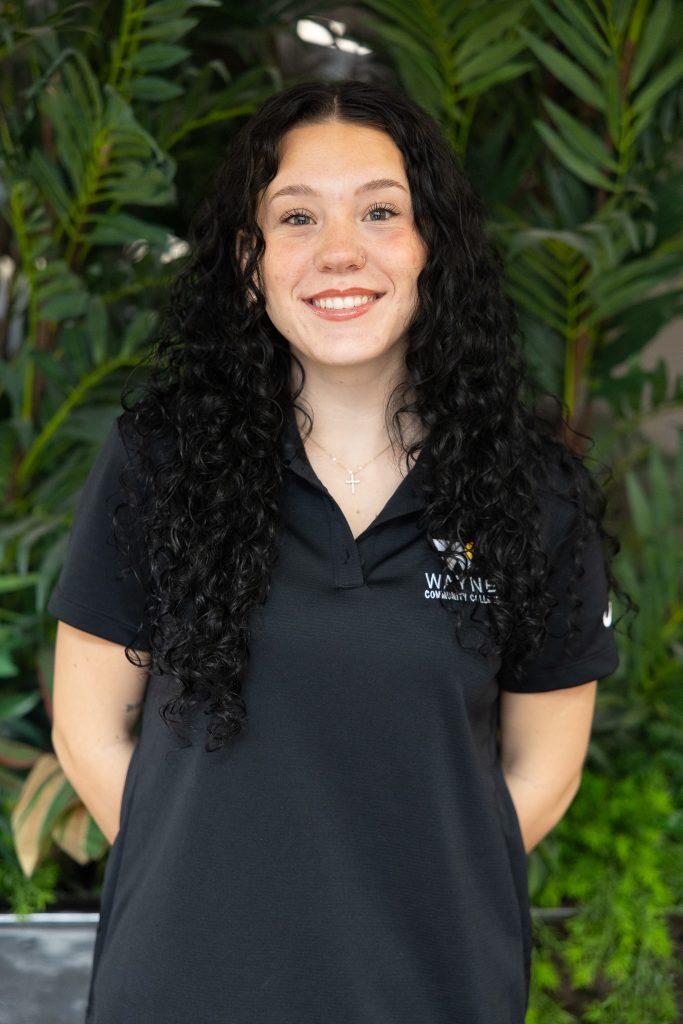A woman stands with her hands behind her back.