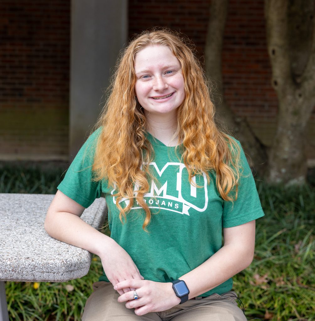 A woman wearing a green T-shirt sits at an outdoor table.