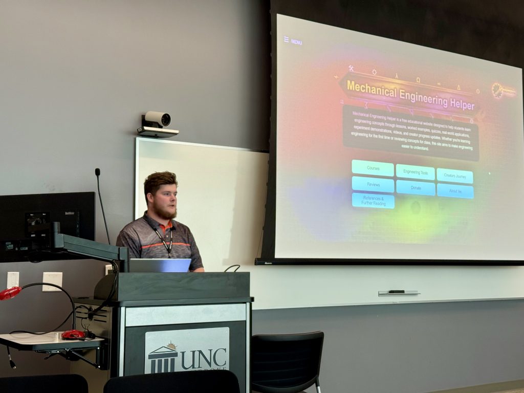 A student stands behind a podium and beside a screen in a classroom.
