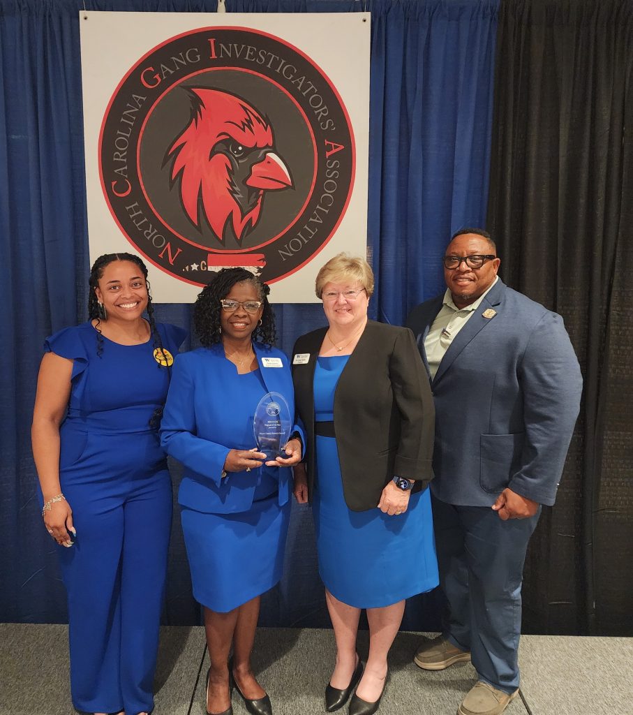 Four individuals stand together, with one person holding a plaque.