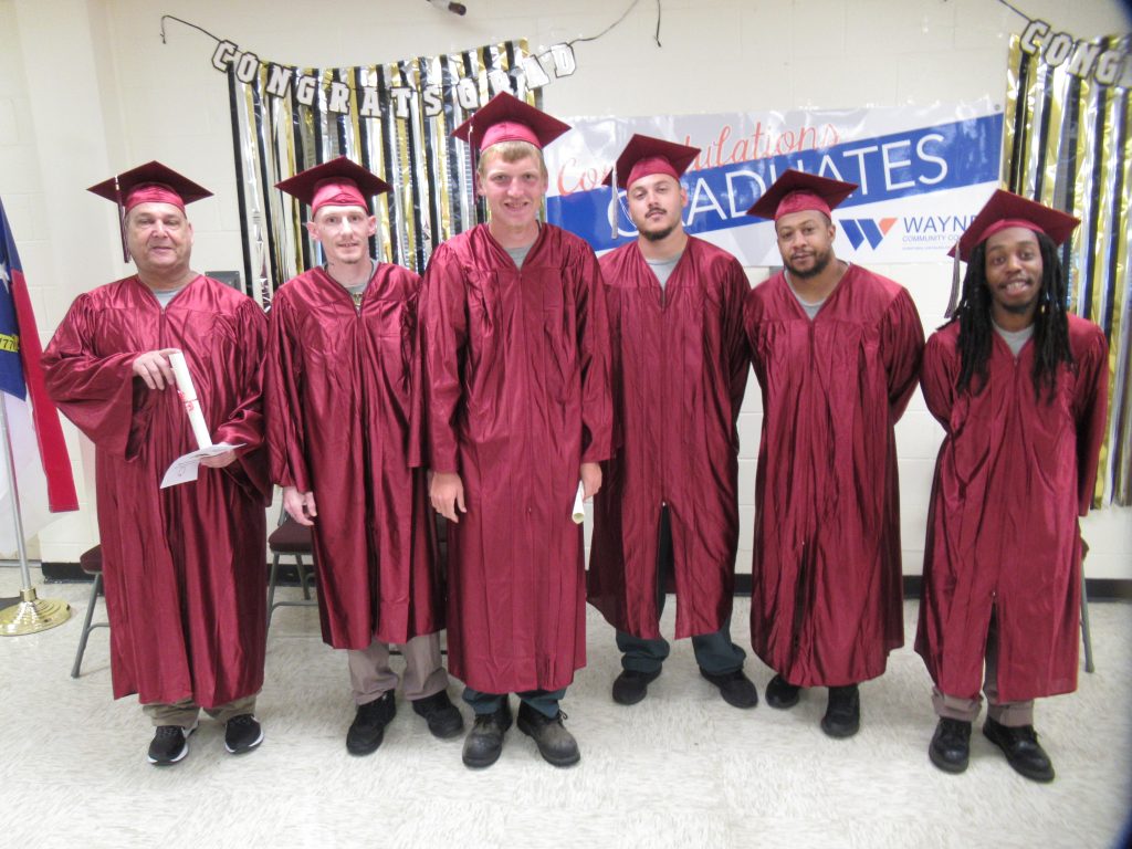 Individuals stand together while wearing red caps and gowns for graduation.