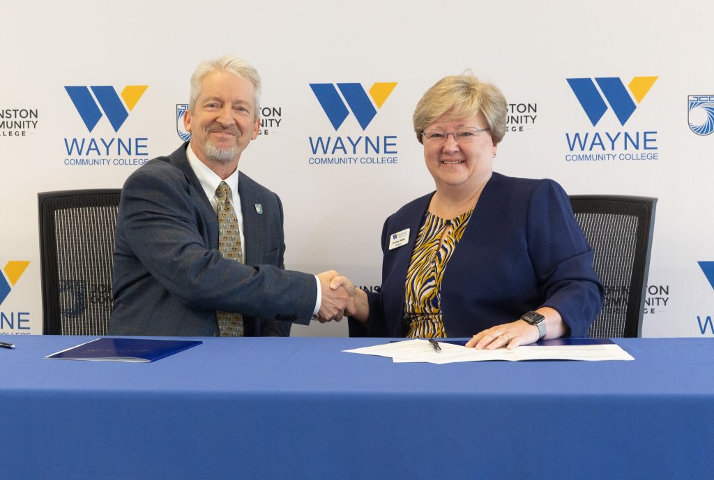A man and woman sit side by side shaking hands and smiling.