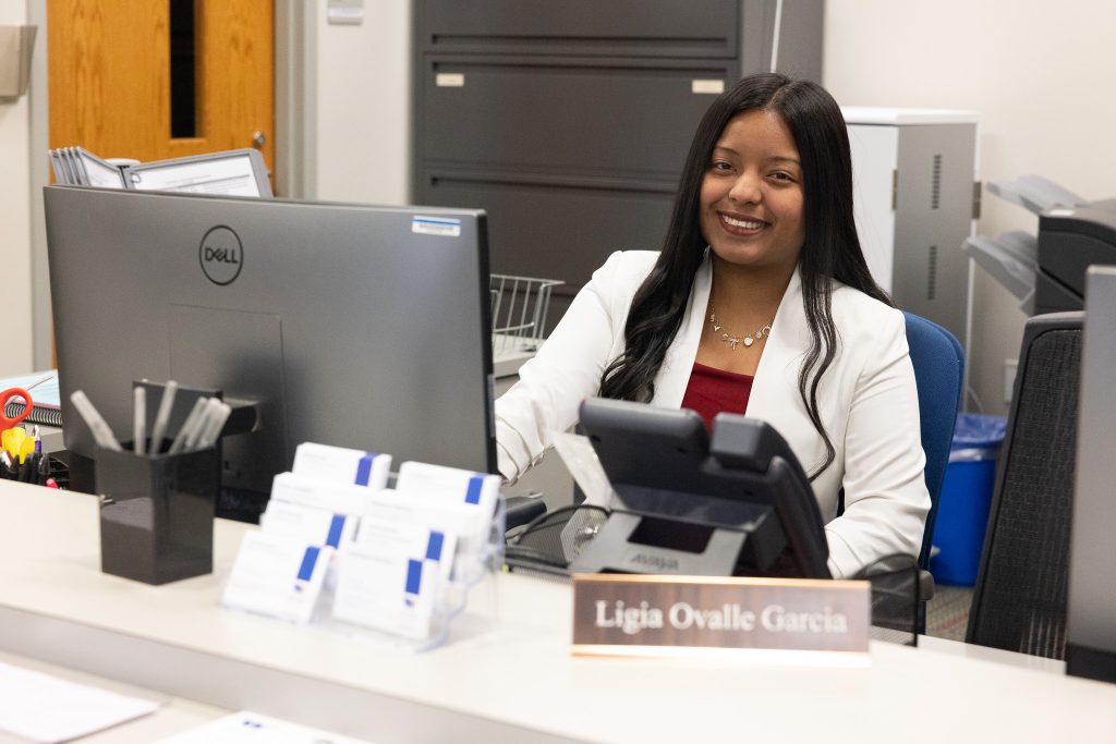 A woman sits at a desk in front of a computer.
