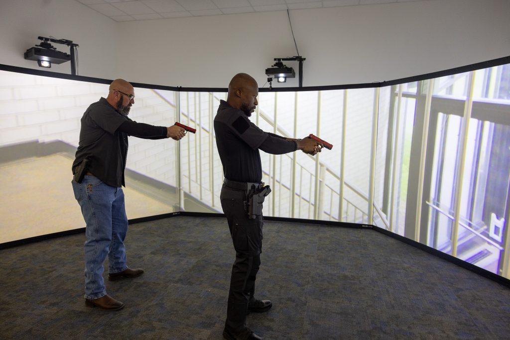 Two individuals stand holding training guns in a simulation lab.