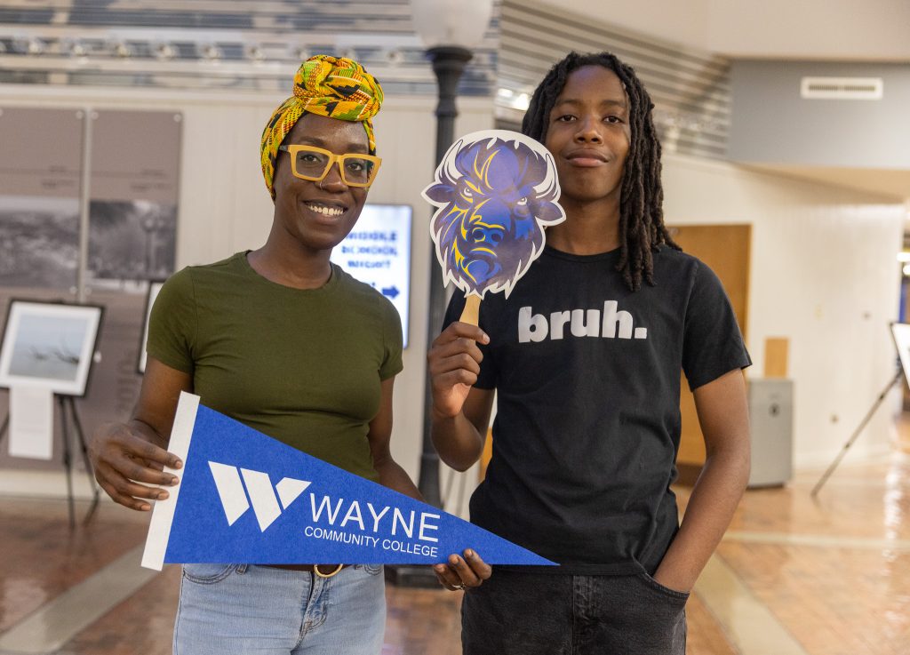 A woman and her son hold a school pennant and a fan of the school mascot.