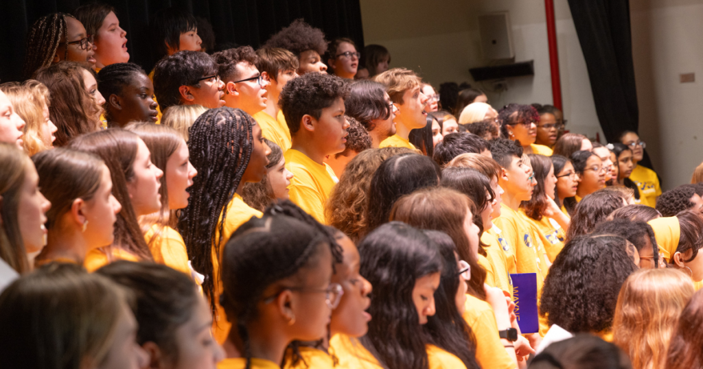 Students wearing yellow T-shirts stand together and sing.