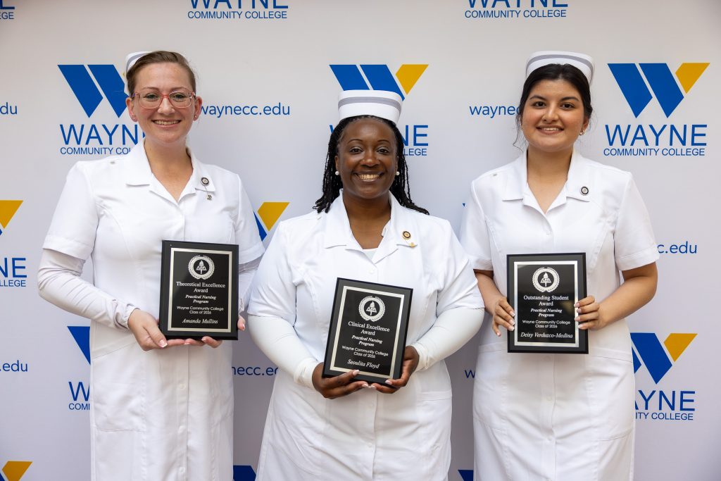Three nurses wearing traditional white nursing uniforms stand together holding plaques.