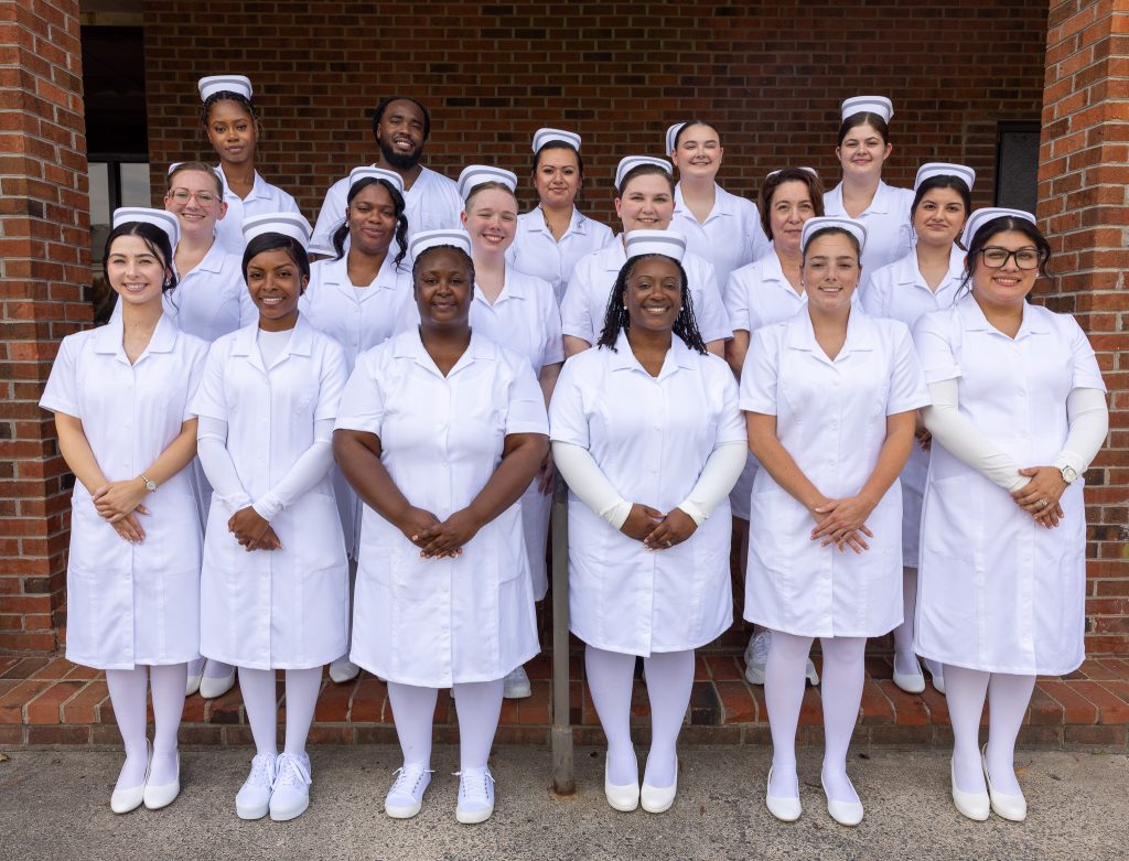 A group of nurses stand together wearing traditional white nursing uniforms.