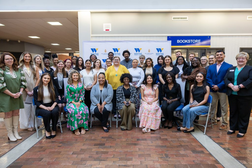A group of individuals stand together with several sitting in chairs in the front.