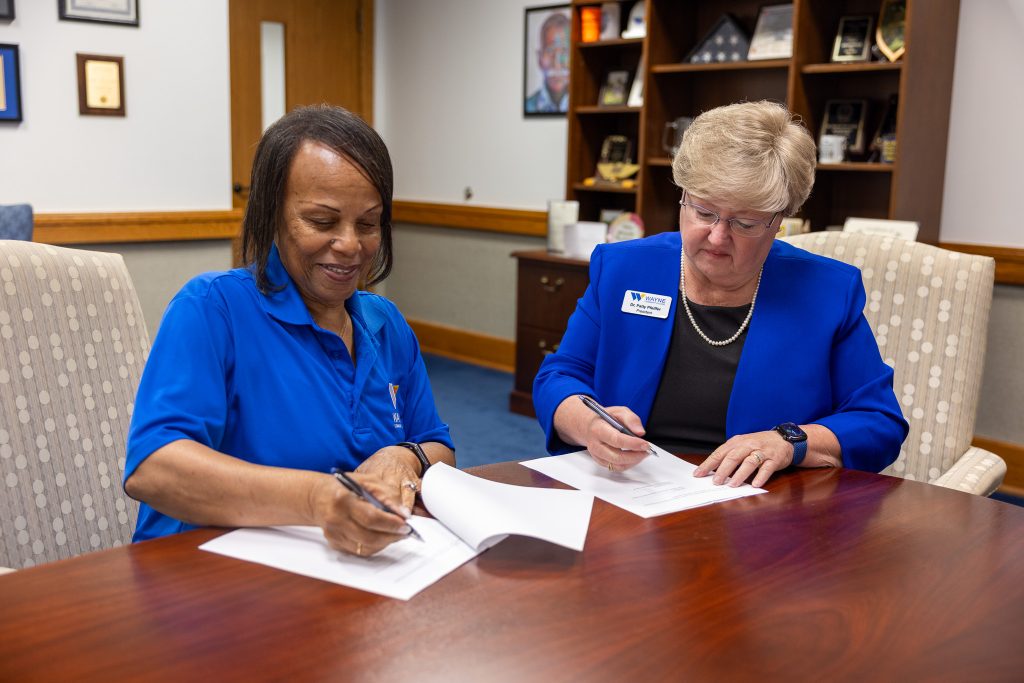 Two women sit at a table signing documents.