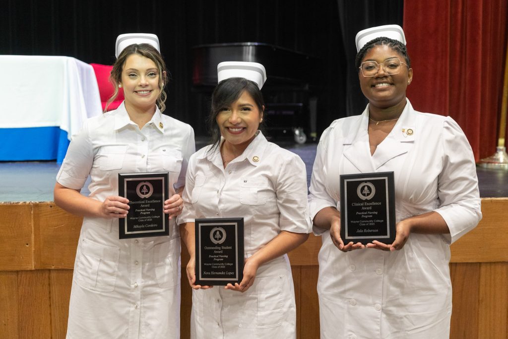 Three women stand together holding plaques while wearing traditional nursing uniforms.