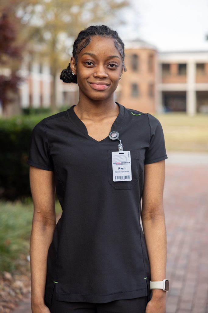 A woman stands for a photo wearing medical scrubs and a badge.