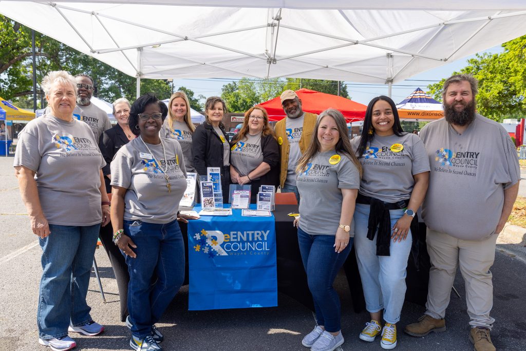 Individuals wearing matching grey T-shirts stand around a table.