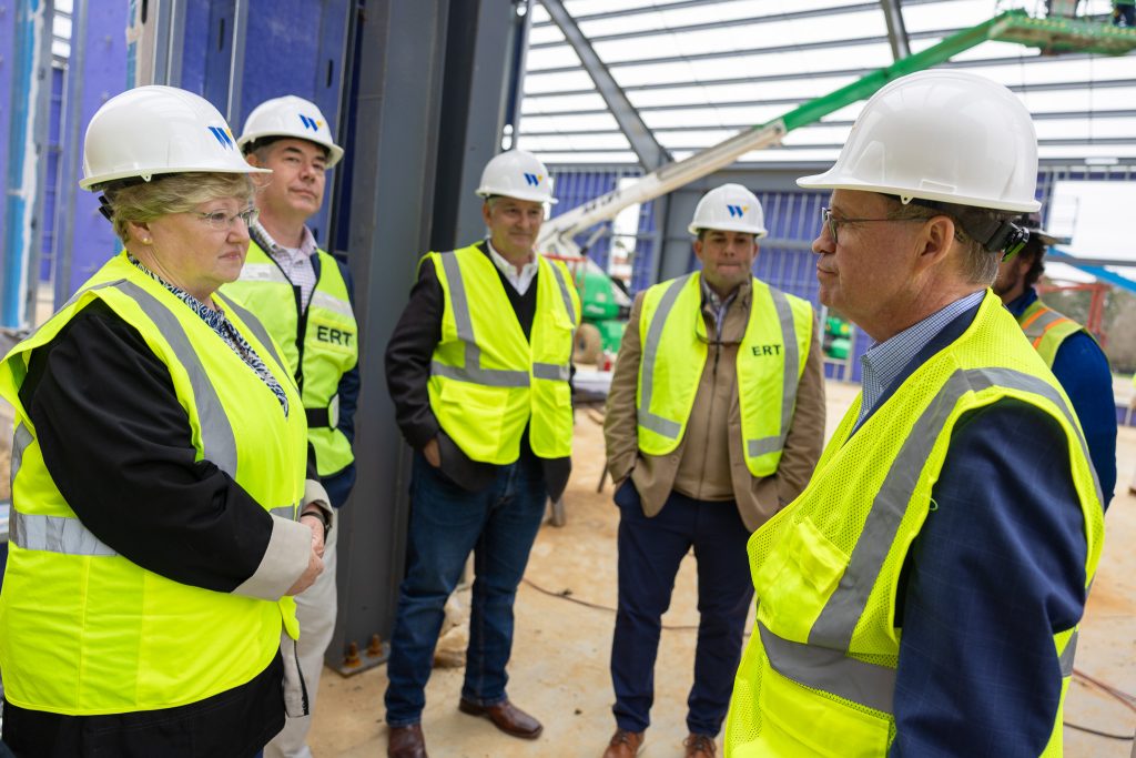 Individuals stand together wearing hard hats and safety vests.