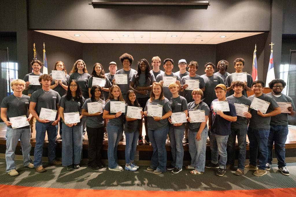 Students stand together holding certificates.