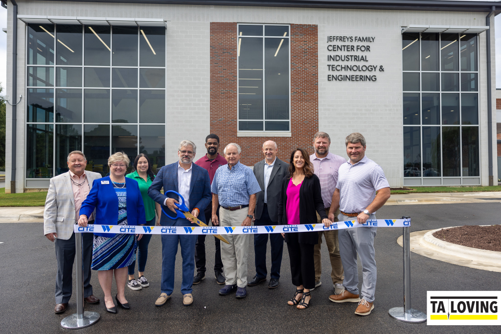 Individuals stand in front of a building while one man holds scissors to cut a ribbon.