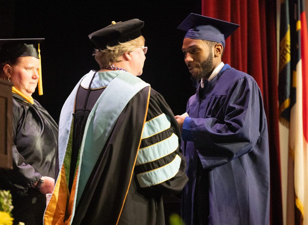A man wearing a graduation cap and gown stands next to a woman wearing a cap and gown.