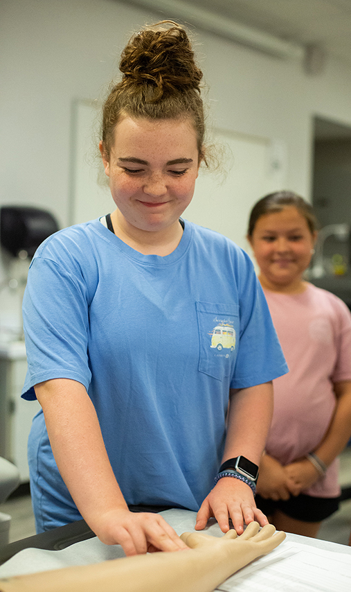 A camper practices taking a pulse using a training arm.