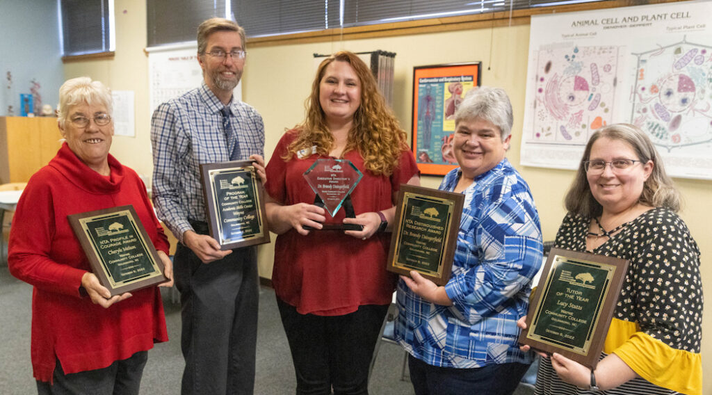 A group of standing people holding plaques and trophies.