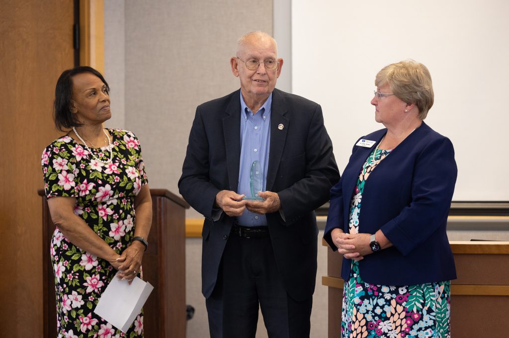 A man holds a plaque while two women stand beside him.