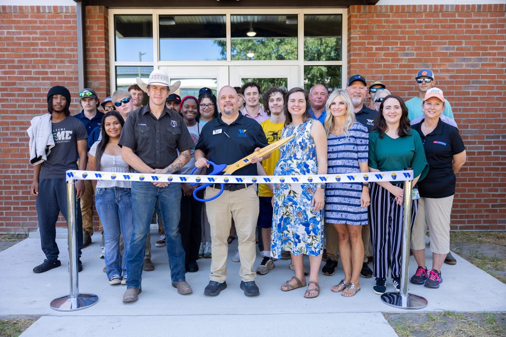 Individuals stand behind a ribbon in front of a building.